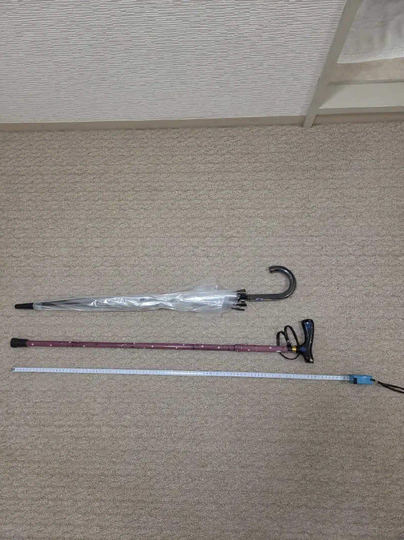 折りたたみ杖とビニール傘を壁に立てかけて長さを比較。杖の方が3〜4cm程度長い